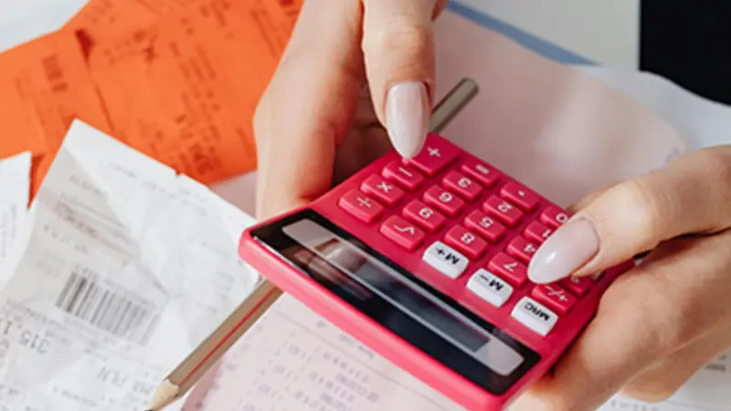 Someone holding a calculator over a stack of bills. 